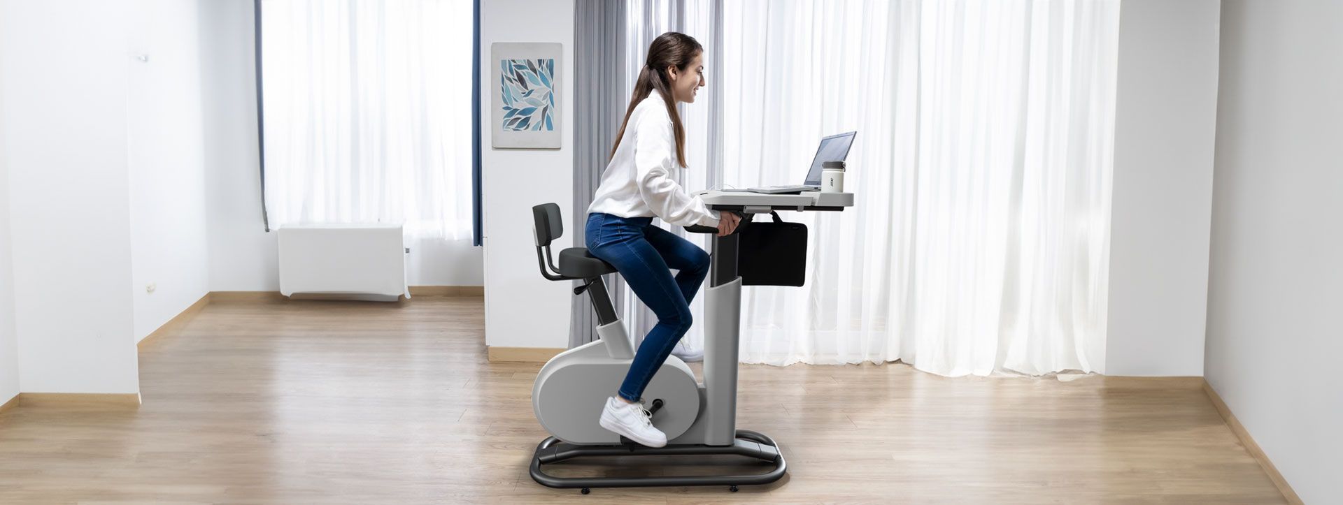 Une femme utilise un vélo stationnaire avec un ordinateur portable installé dessus dans une pièce.