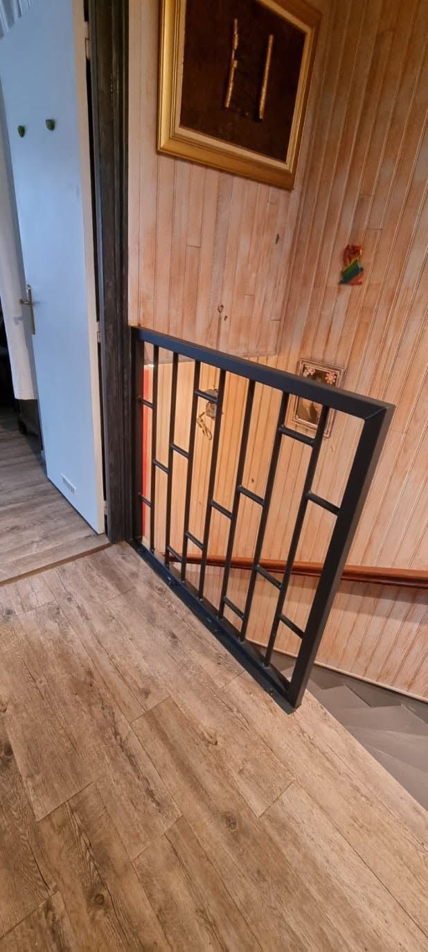 Panneau de portail en métal noir appuyé contre un mur lambrissé dans un couloir