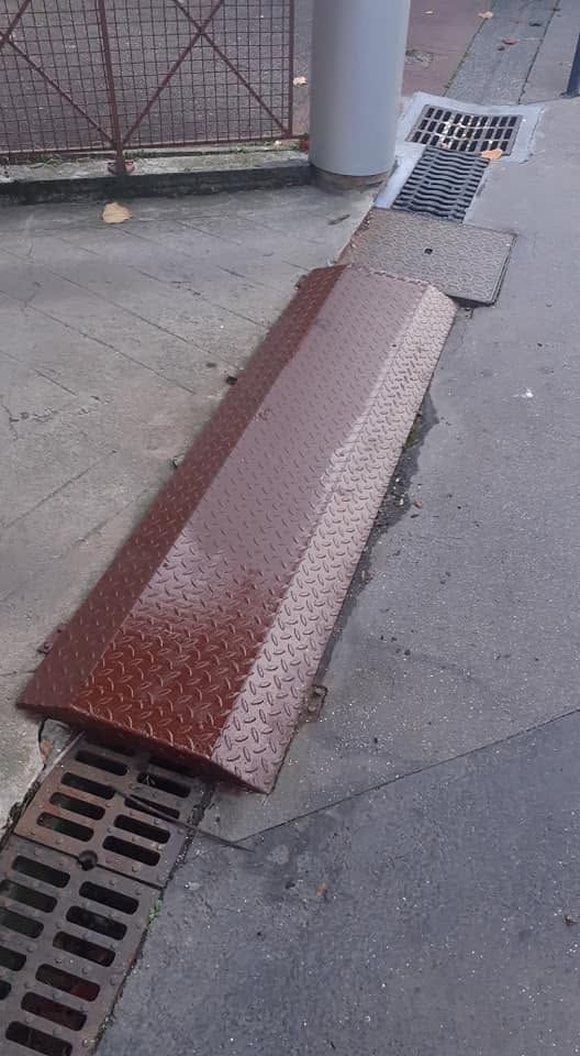 Rampe de trottoir en métal plié au-dessus d’une bouche d’égout pluvial, avec un revêtement blanc et couleur rouille