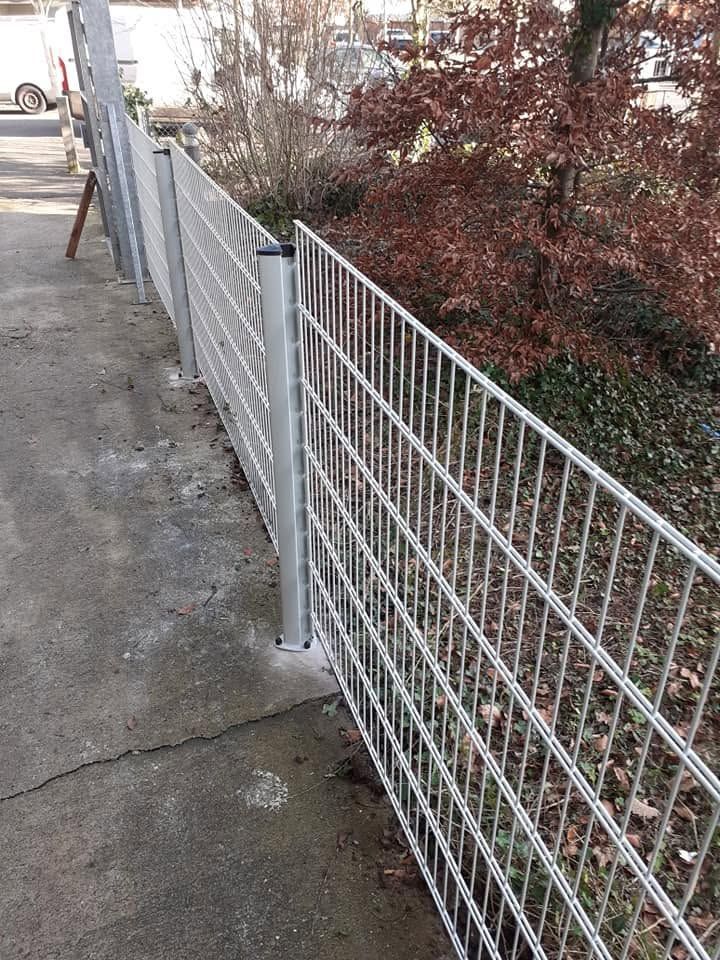Clôture métallique longeant un trottoir, à côté d’un mur de briques et de buissons