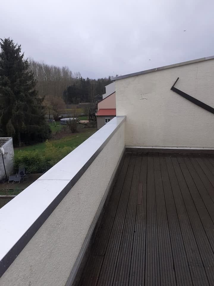 Terrasse sur le toit avec parapet blanc, sol sombre et ciel nuageux surplombant un paysage boisé