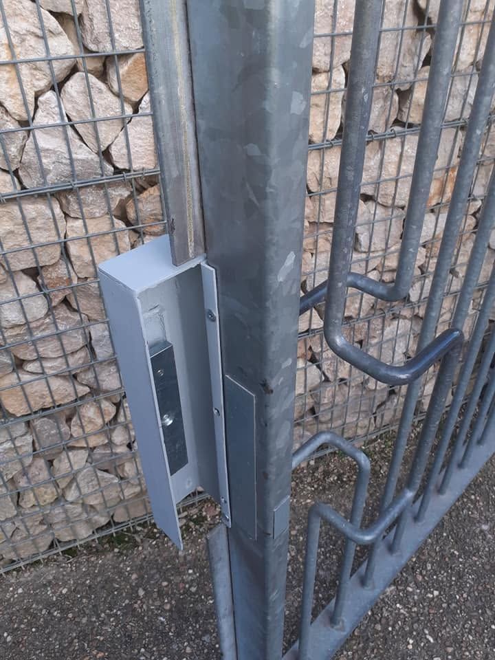 Loquet métallique monté à côté d’une clôture en fil de fer et d’un mur en pierre, à l’extérieur