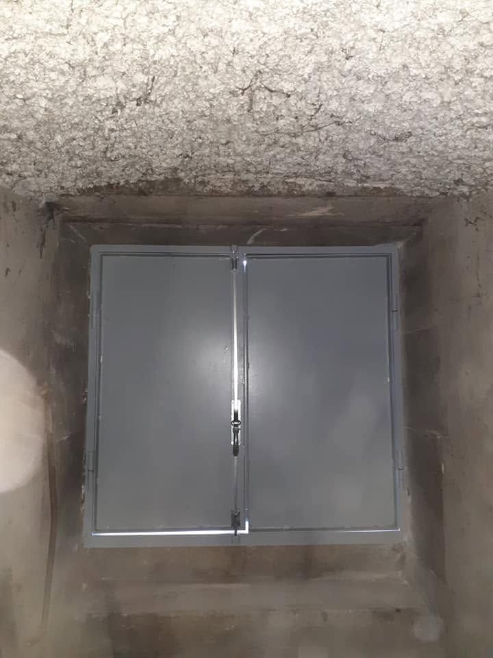 Petite fenêtre double grise encastrée dans une niche creusée dans un mur de béton brut