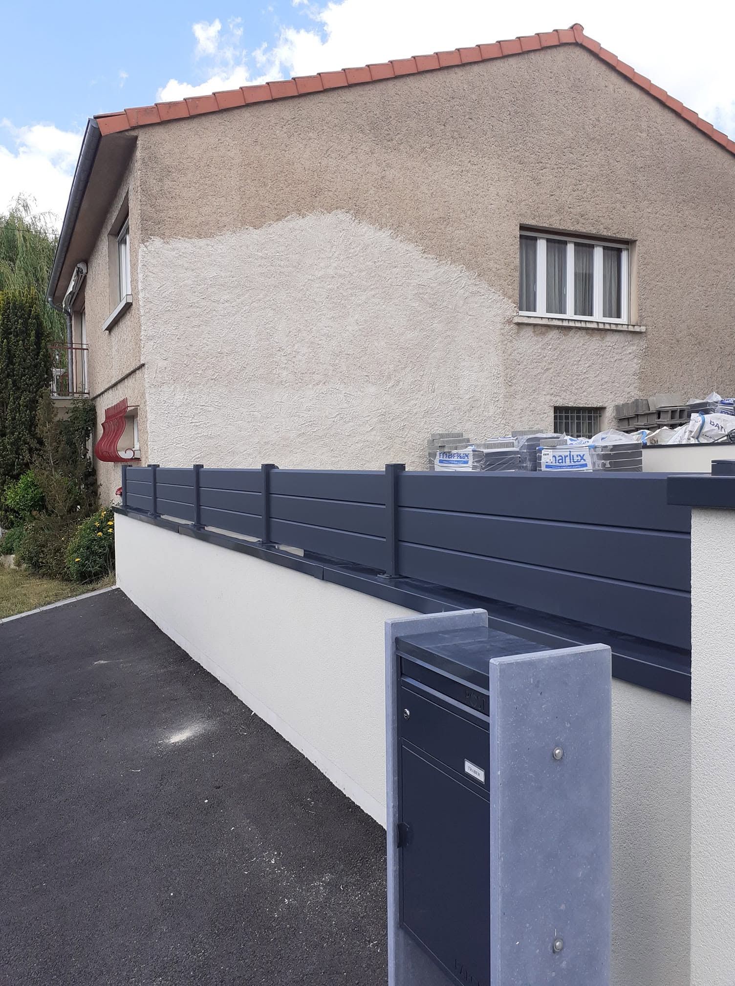 Maison résidentielle aux murs en stuc blanc, avec une clôture bleue et une boîte aux lettres grise le long d’une allée pavée