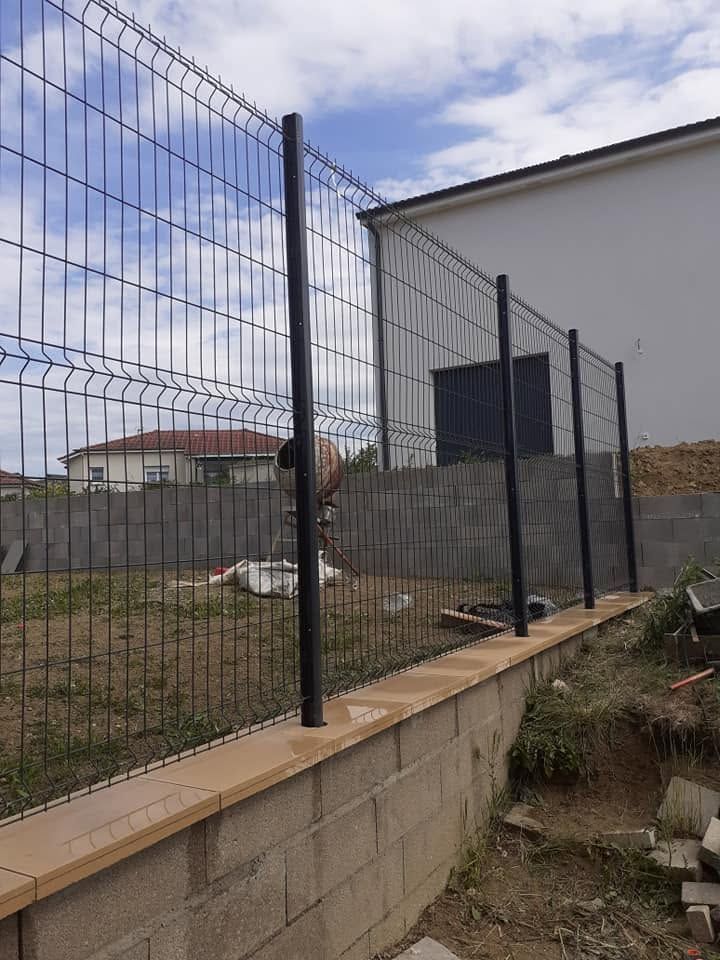 Clôture métallique le long d’un mur en parpaings, à côté d’un bâtiment blanc et d’une cour gazonnée