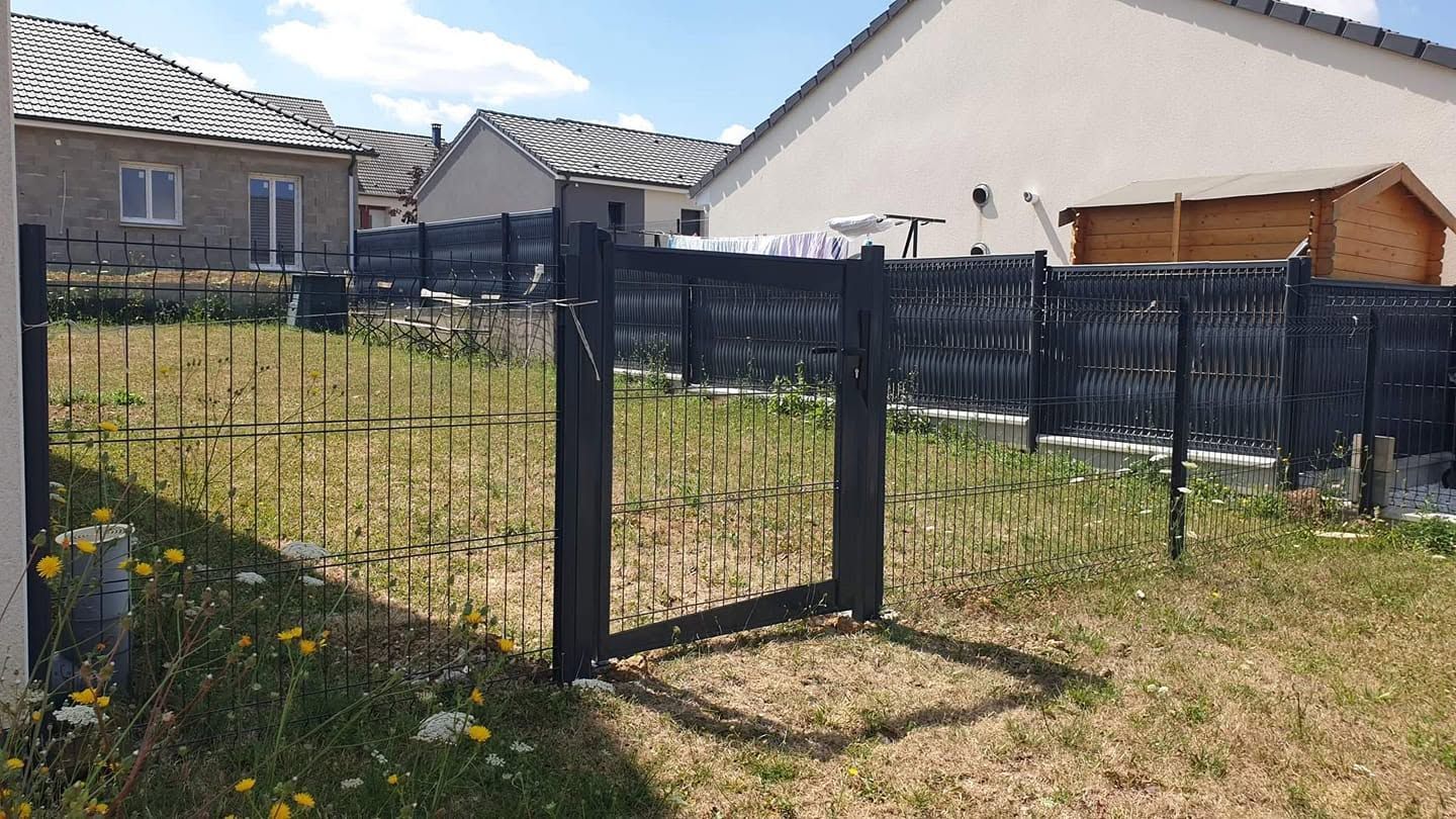Clôture et portail en métal noir autour d’un jardin avec de l’herbe, des maisons en arrière-plan