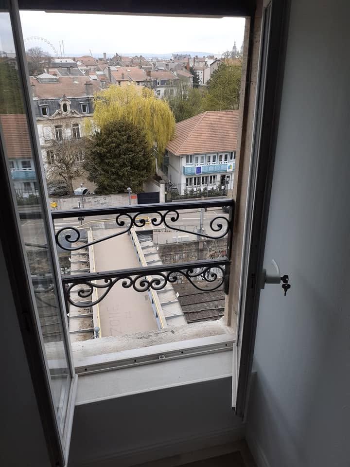 Vue depuis une fenêtre donnant sur une cour et des toits, avec une élégante balustrade de balcon noire au premier plan