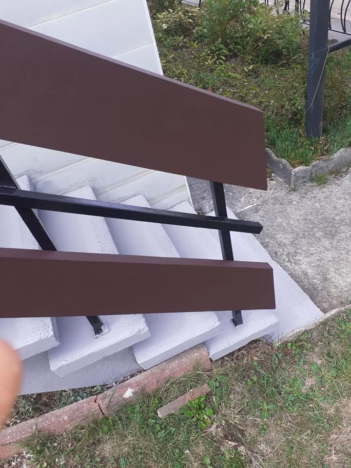Des panneaux de clôture marron et des emballages en mousse blanche appuyés contre un trottoir, à côté d’herbe et de gravier.