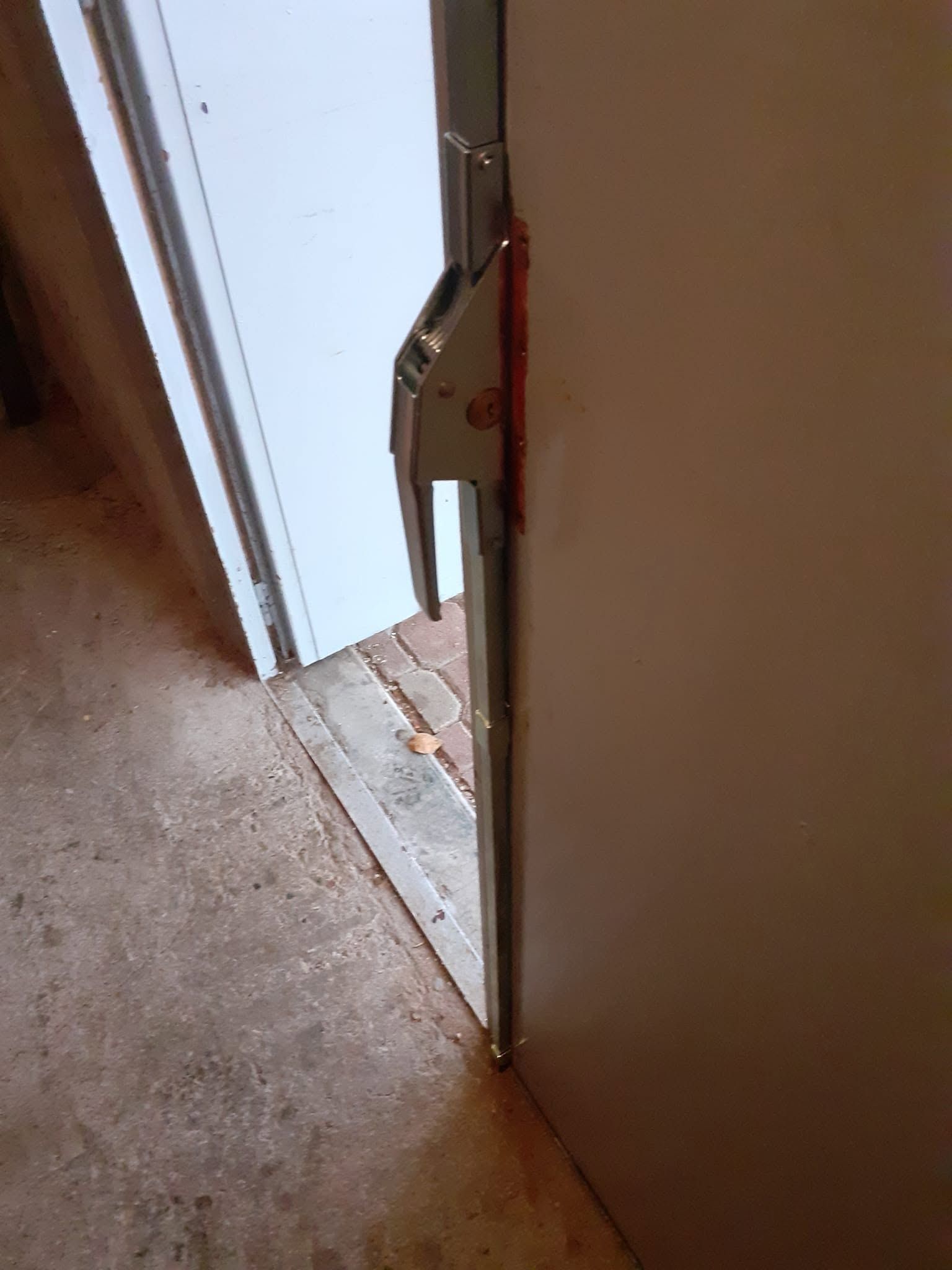 Porte ouverte avec un loquet argenté, laissant voir un encadrement de porte blanc et le sol moquetté du couloir.