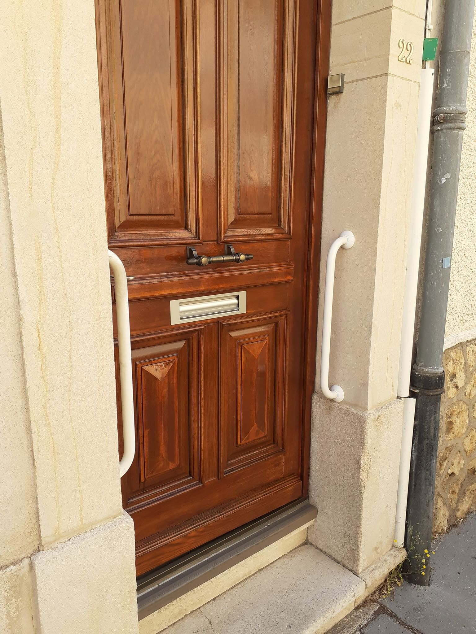 Porte d’entrée en bois avec des rampes blanches, encastrée dans une ouverture en pierre.