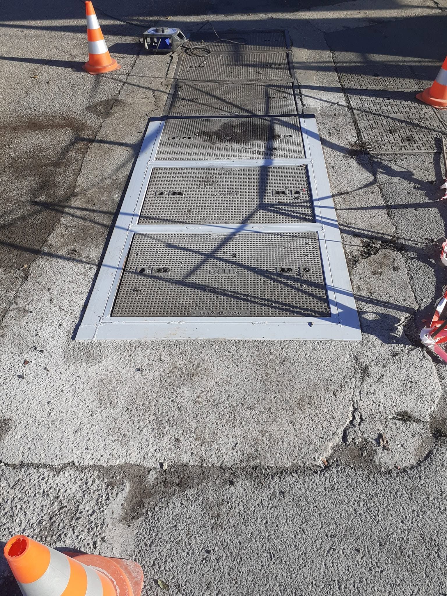 Grille métallique surélevée au-dessus d’une route goudronnée, entourée de cônes de signalisation.
