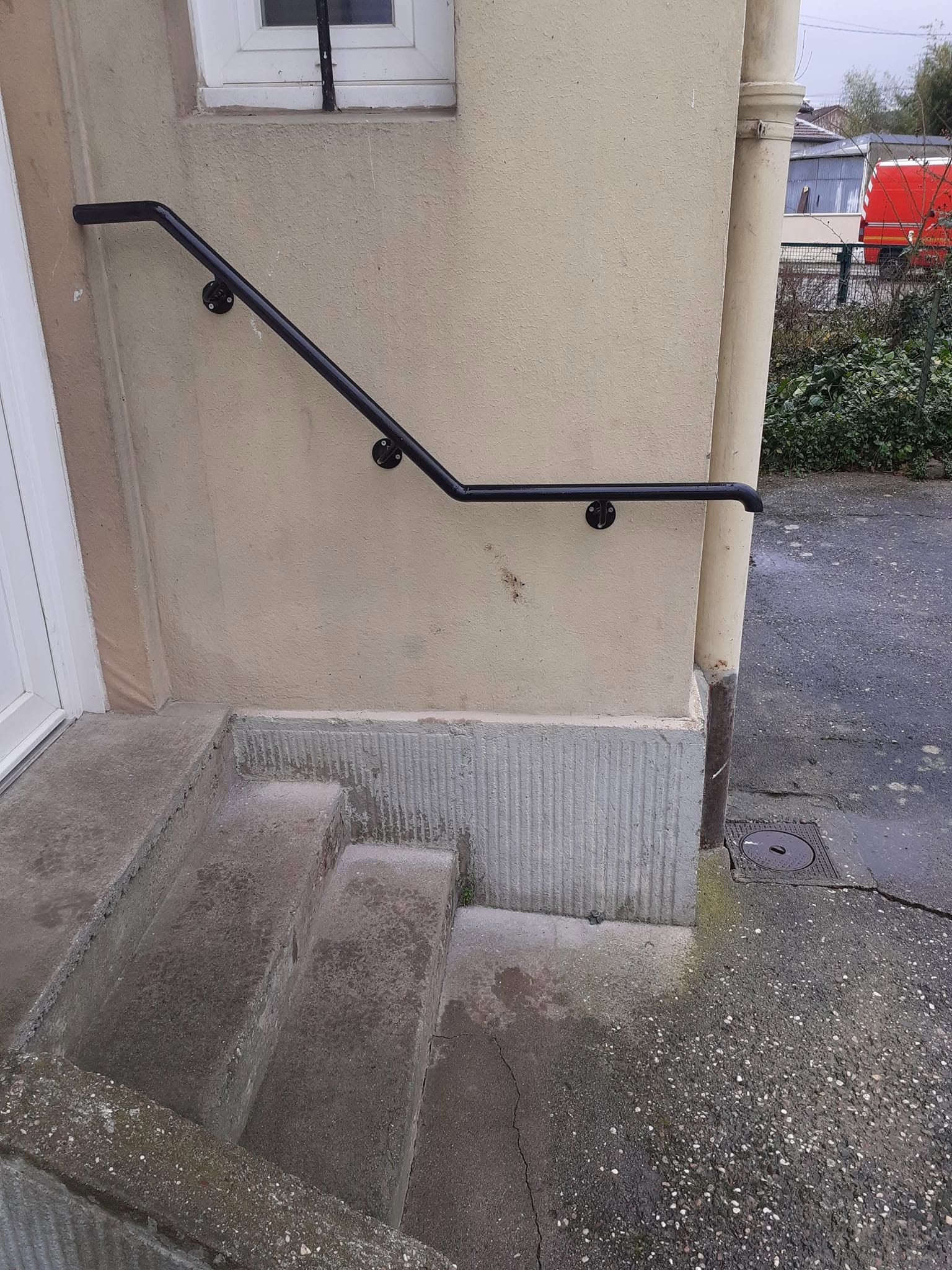 Des marches extérieures avec une rampe noire menant à l’entrée d’un bâtiment beige