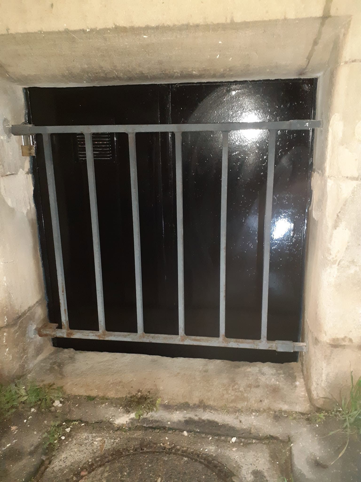 Petite fenêtre de sous-sol à barreaux, encastrée dans un mur en béton, la nuit.