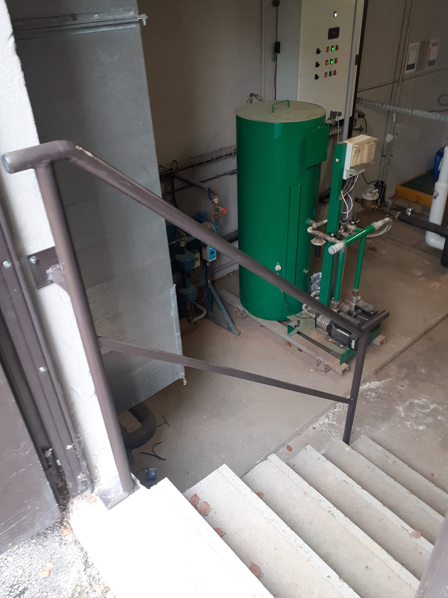 Cage d’escalier avec des rampes et une cuve industrielle verte dans un local technique