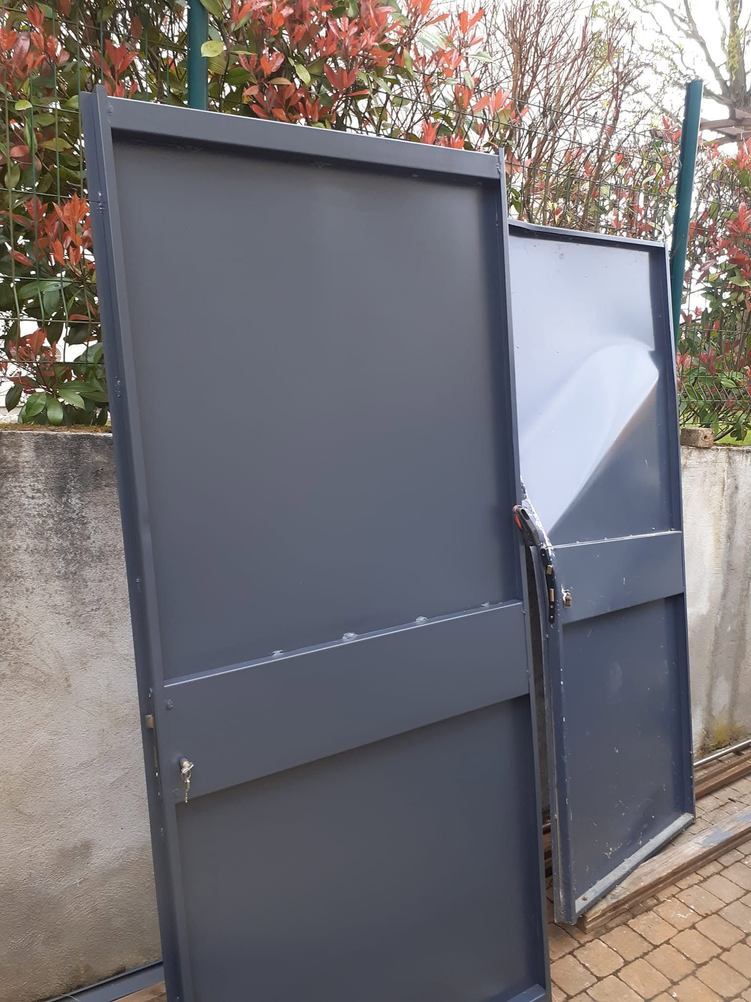 Deux portails en métal noir, ouverts en appui contre un mur à l’extérieur