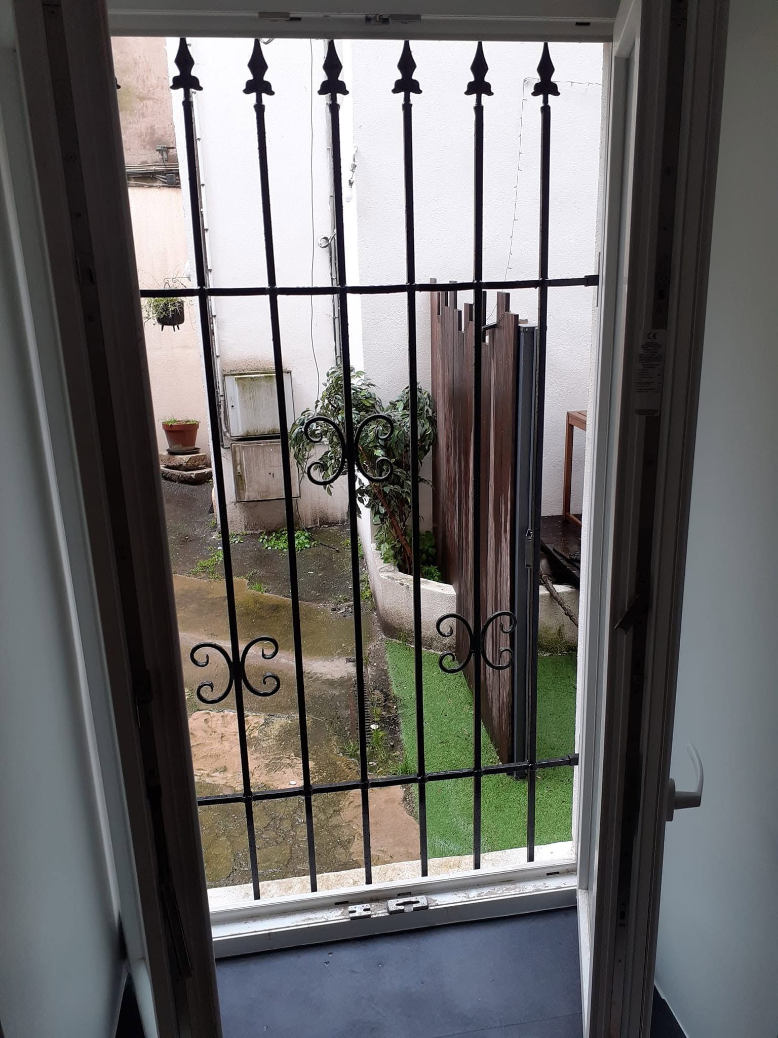 Vue à travers une porte à barreaux sur une petite cour avec des plantes en pot et une parcelle de gazon