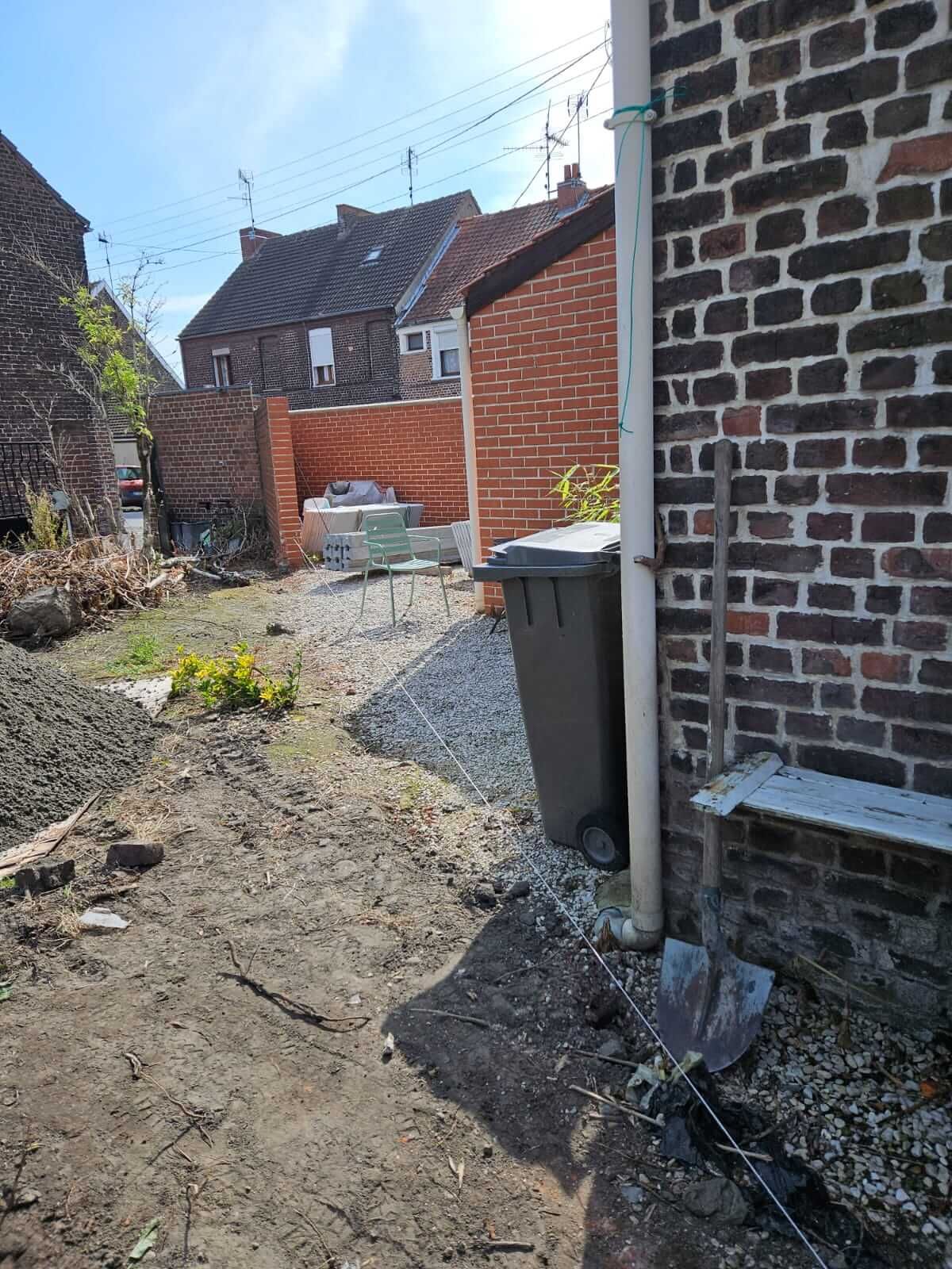 Aménagement extérieur avec un jardin en cours de réalisation, présence d'un bac de tri et d'un mur en briques