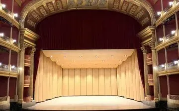 Escenario de teatro vacío con cortinas rojas, detalles dorados y fondo beige.