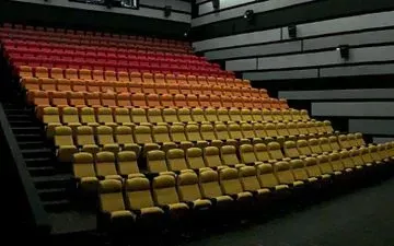 Auditorio de cine vacío con filas escalonadas de asientos de color amarillo y rojo, paredes laterales negras y una escalera.