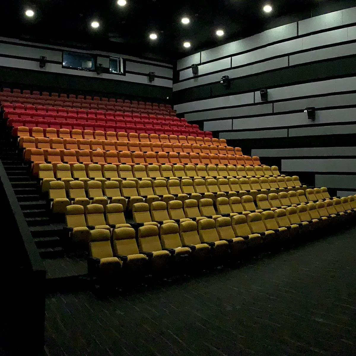 Auditorio de cine vacío con filas de butacas amarillas y rojas. Paredes oscuras y techo iluminado.