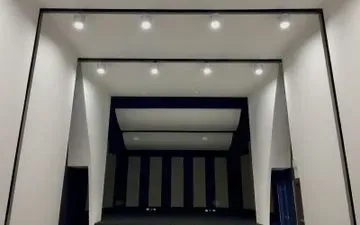 Vista interior de un pequeño auditorio o escenario, pintado principalmente en blanco y azul oscuro, con luces brillantes en el techo.