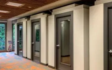 Pasillo con varias puertas cerradas. Las puertas tienen marcos oscuros y paneles de vidrio, colocadas en nichos blancos en las paredes.