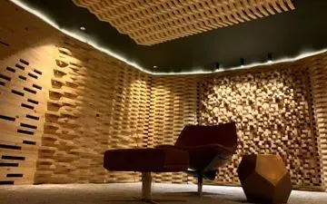 Un estudio de grabación moderno con paredes y techo de madera texturizada. Una silla roja se encuentra en el centro, iluminada por un perímetro de luces.