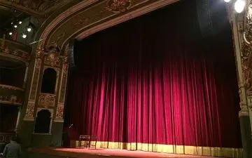El telón de terciopelo rojo se cerró en un gran teatro ornamentado. Iluminación tenue.