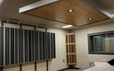 Interior de estudio de grabación: Paneles acústicos en rayas blancas y negras, madera y paneles montados en el techo para tratamiento de sonido.