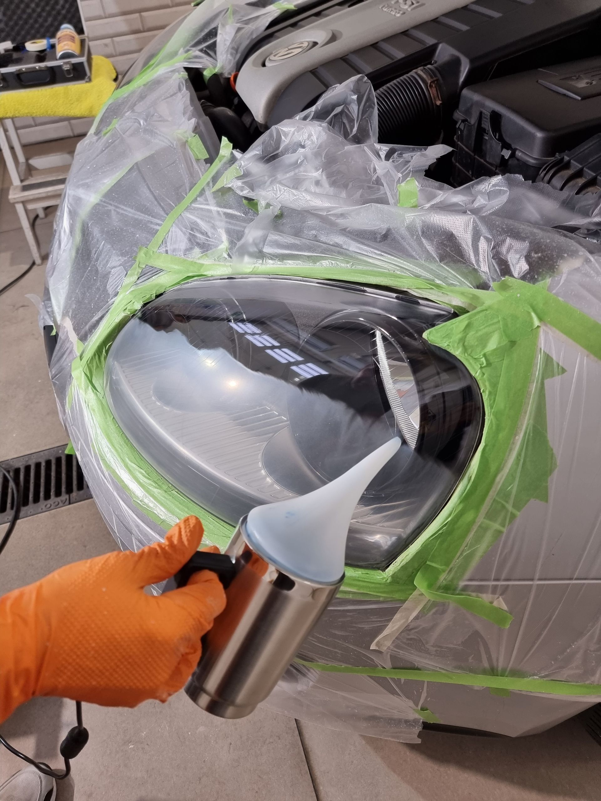 Una persona que lleva guantes de color naranja vierte líquido en el faro de un coche.