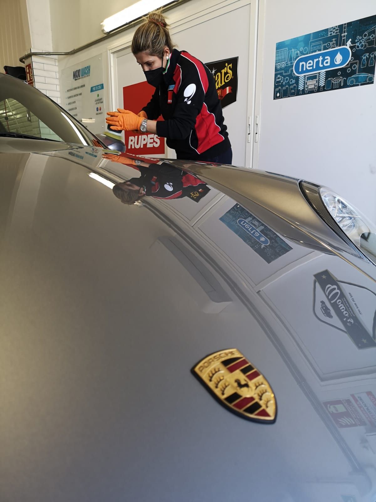 Una mujer está puliendo el capó de un Porsche en un garaje.