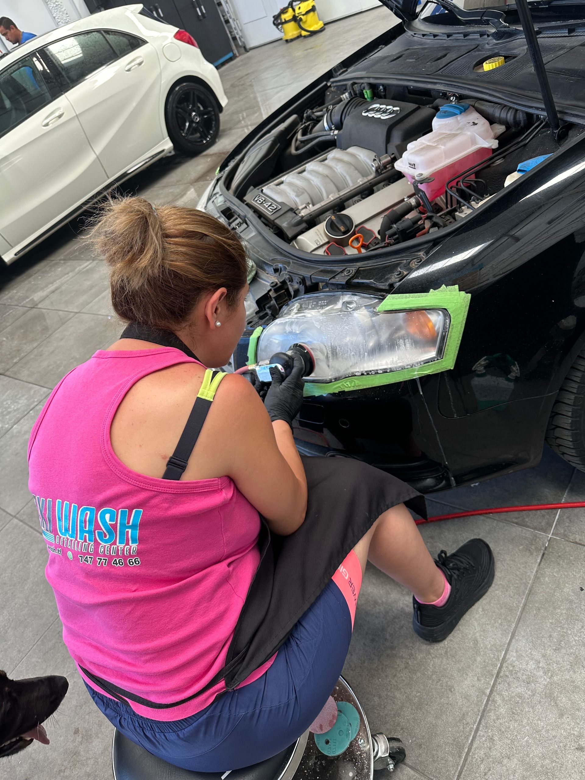 Una mujer está sentada en un taburete puliendo los faros de un coche.