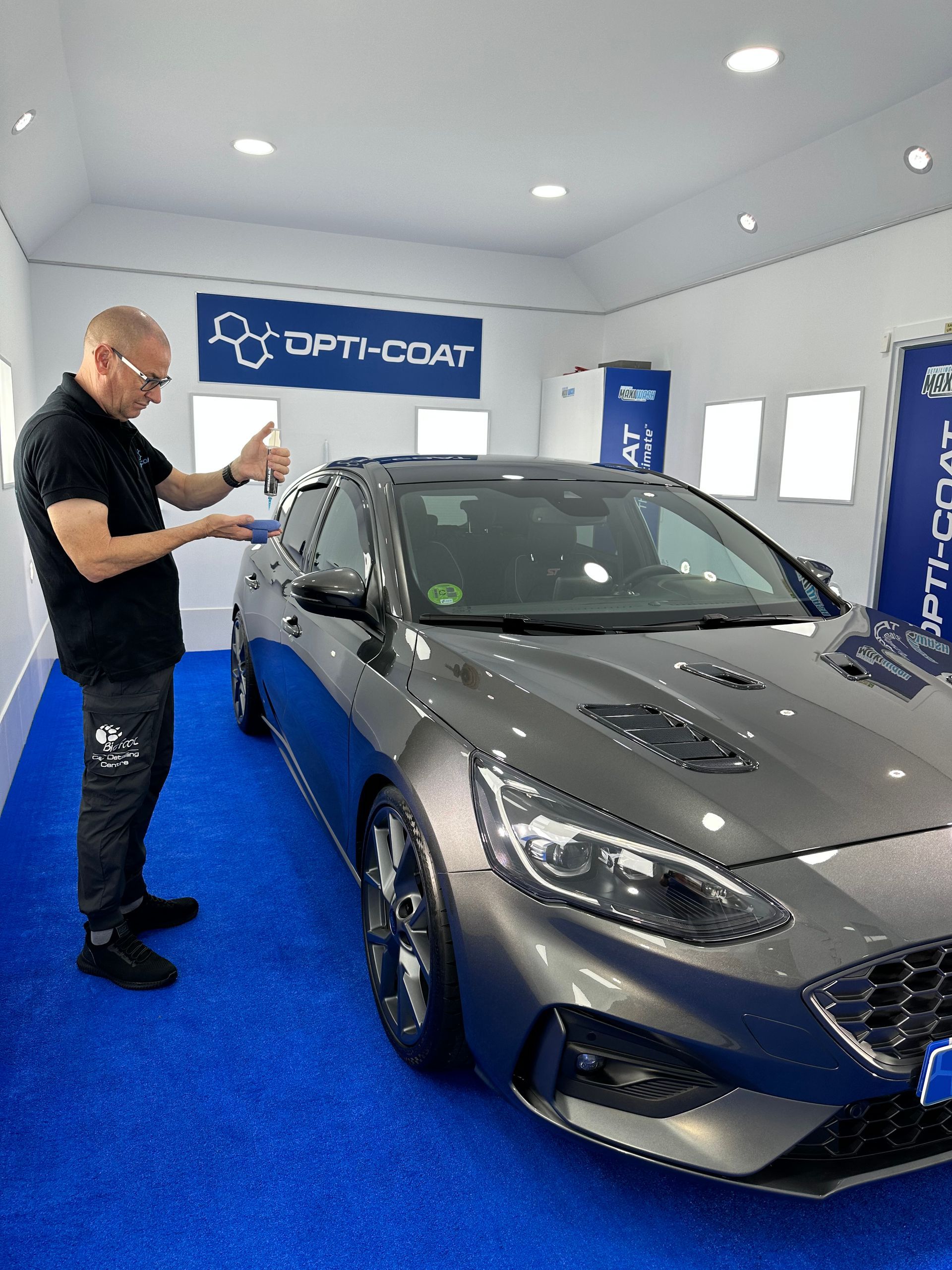Un hombre está de pie junto a un coche en un garaje.