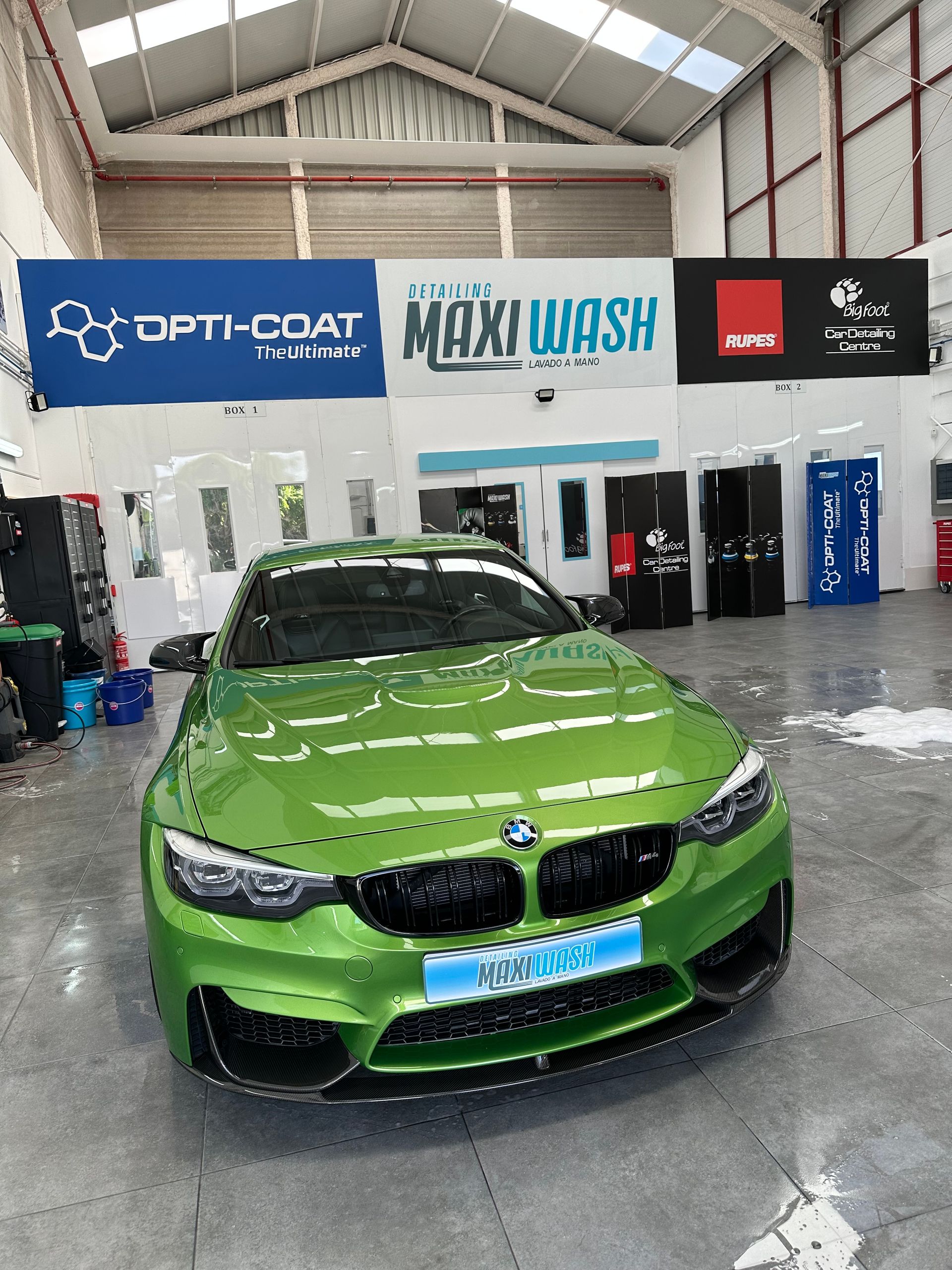 Un coche verde está aparcado delante de un cartel de lavado de coches grandes.