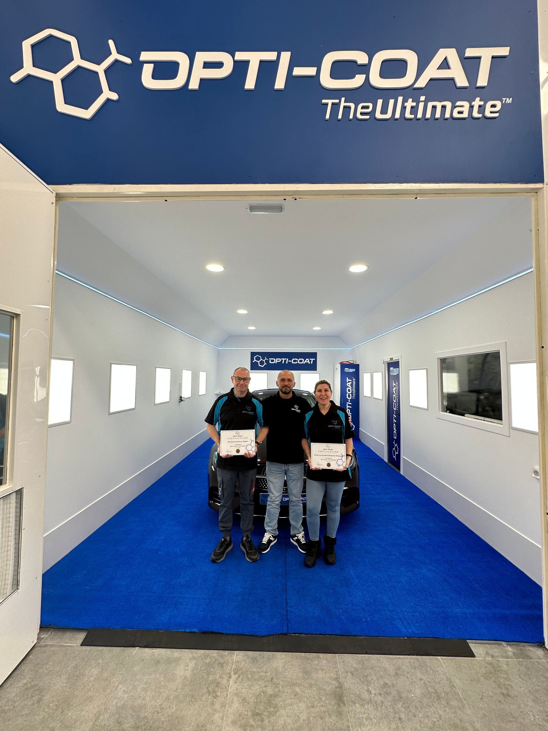 Un grupo de personas de pie delante de un cartel de opti-coat.