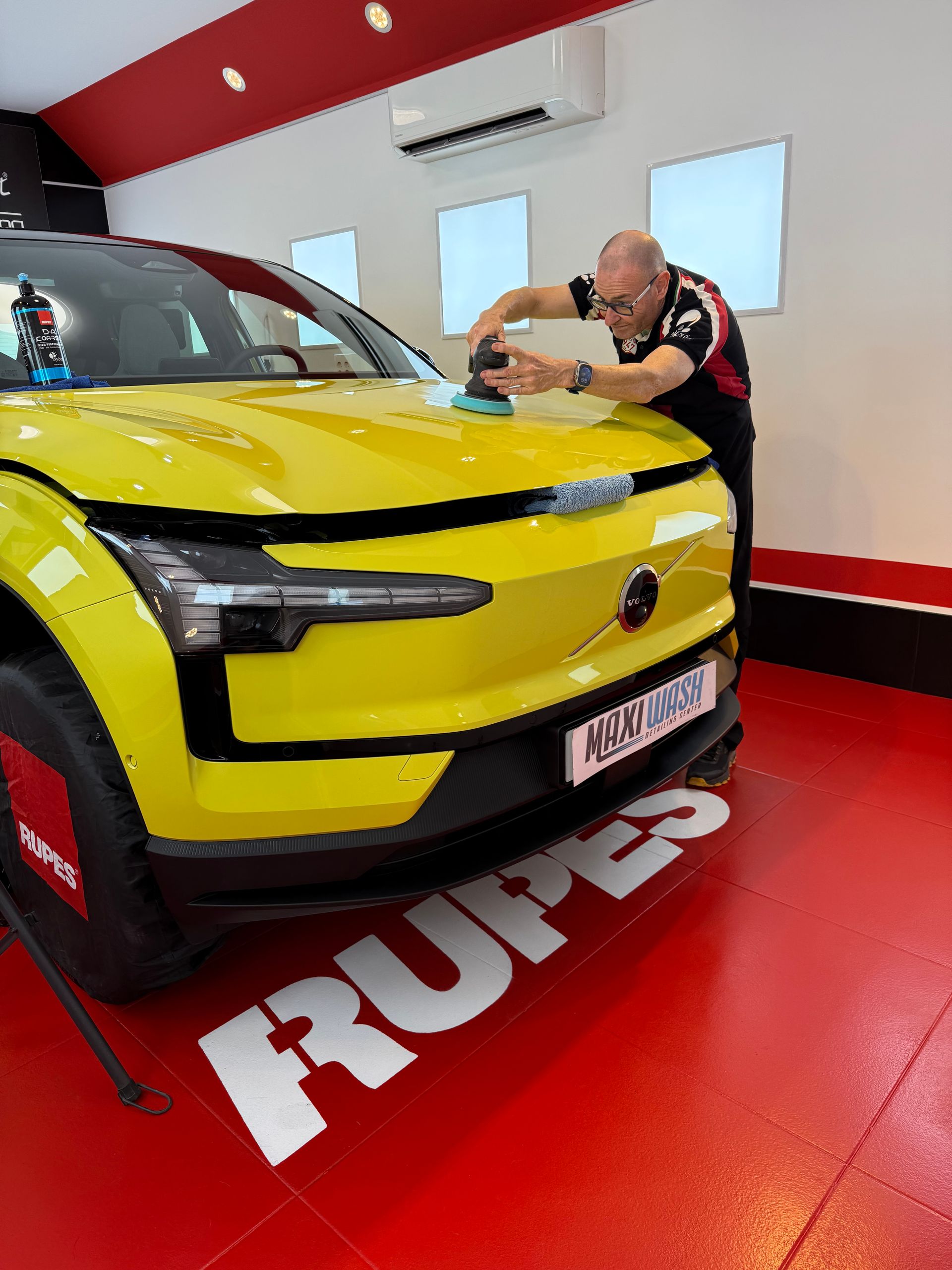 Un hombre está puliendo un coche amarillo en un garaje.
