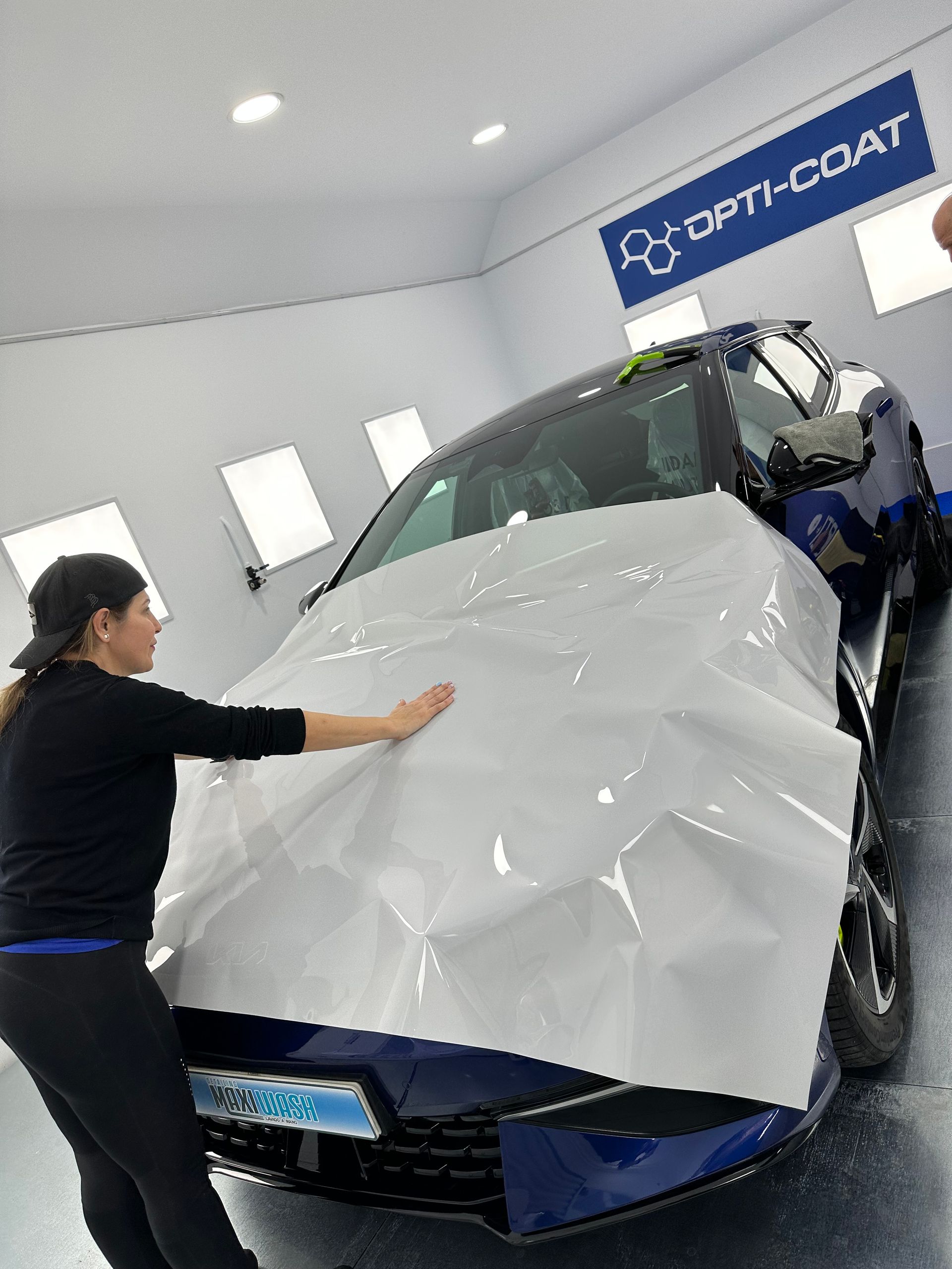 Una mujer está envolviendo un coche azul con vinilo blanco.