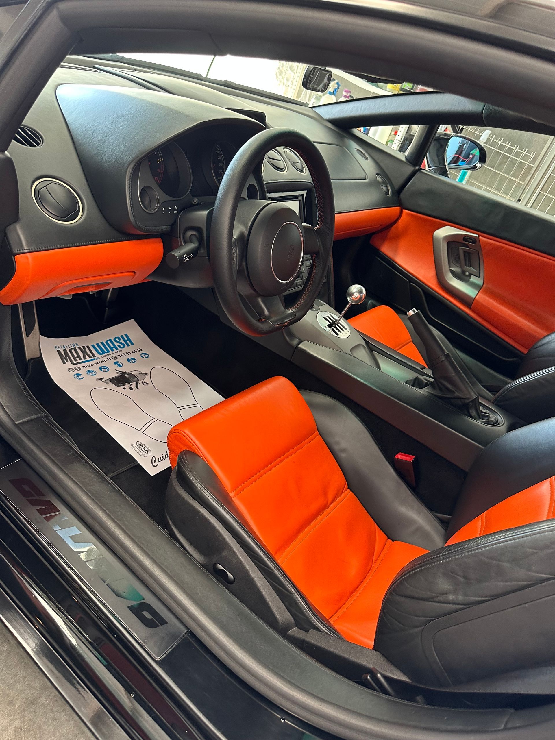 El interior de un coche negro con asientos y volante de color naranja.