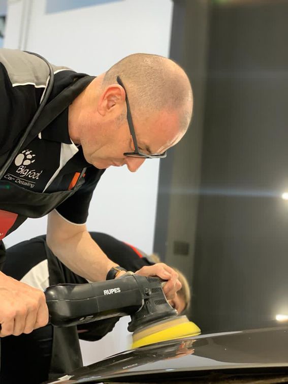 Un hombre está puliendo un coche con una máquina que dice rupo.