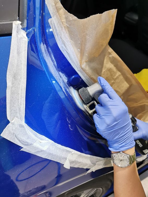 Una persona que lleva guantes azules está puliendo un coche azul.