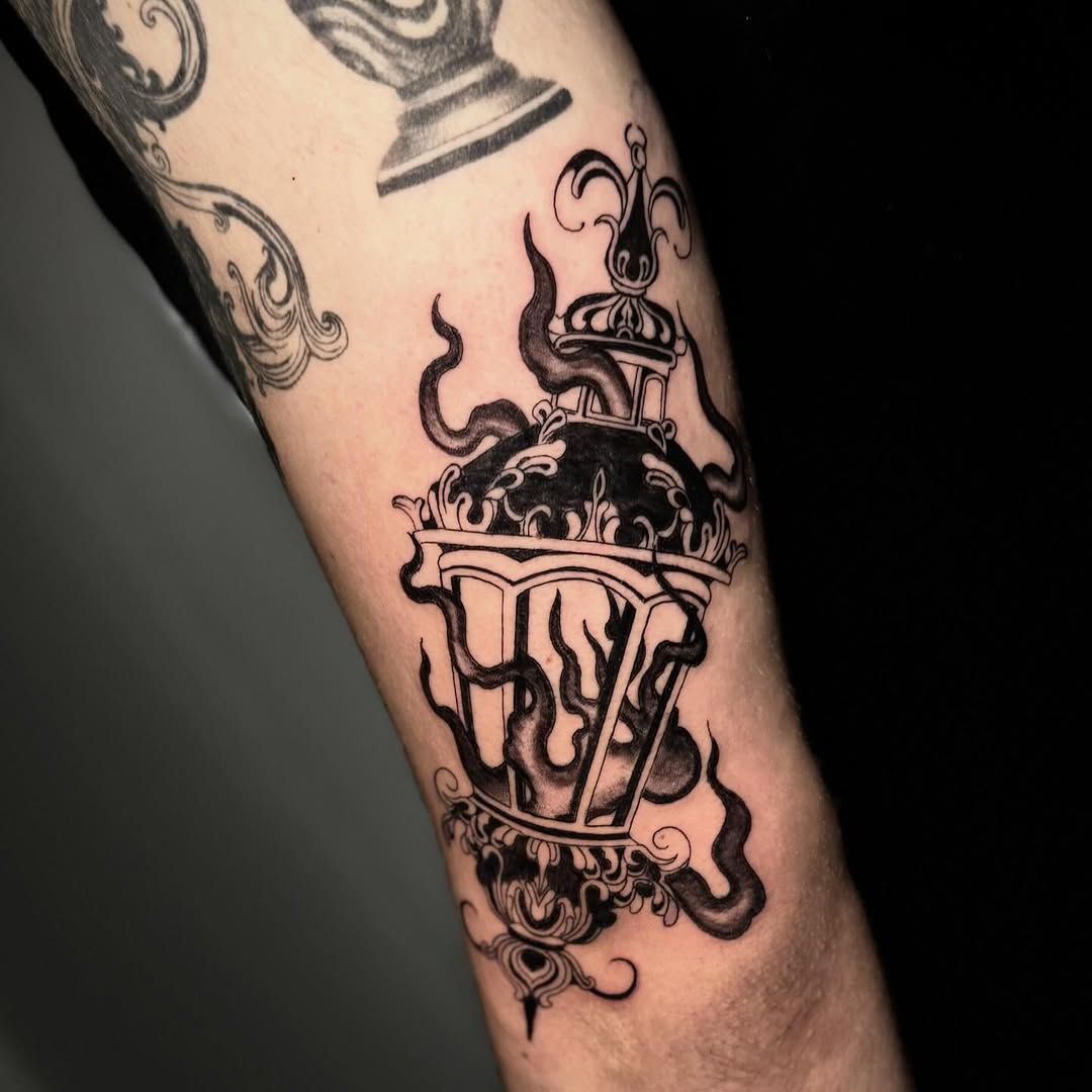 Tatuaje gótico en blanco y negro en el antebrazo con calavera, corona y detalles de goteo.