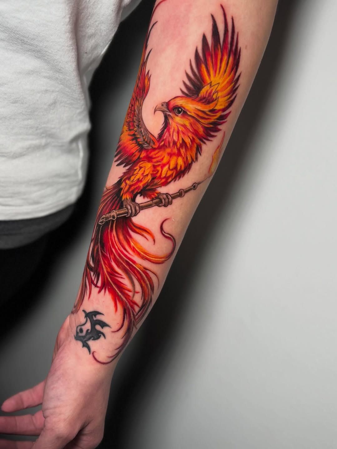 Tatuaje en el antebrazo de una persona: un fénix de color naranja rojizo ardiente.