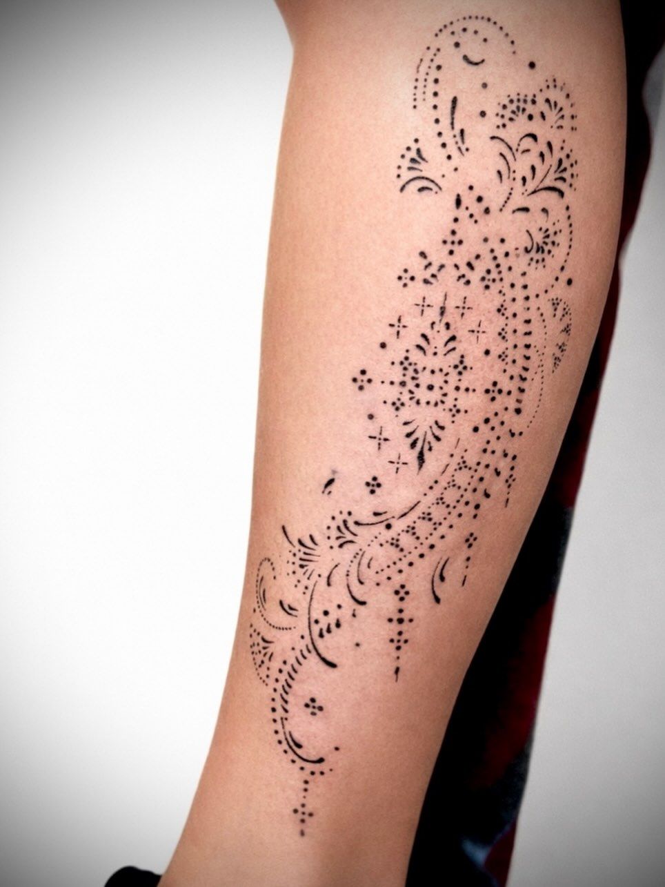 Diseño de tatuaje de henna con motivos florales y punteado en color negro en un antebrazo.