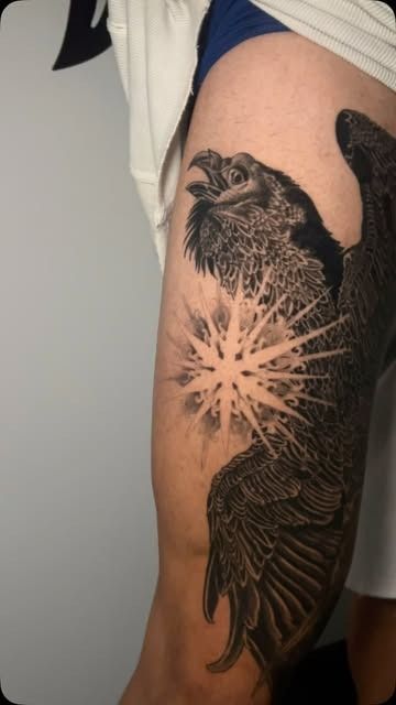 Tatuaje negro de un pájaro y un diseño de explosión estelar en la parte superior del brazo de una persona.
