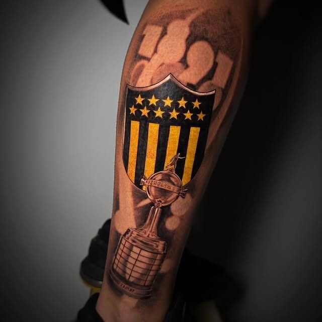 Tatuaje de rayas negras y amarillas con cinco estrellas y un diseño similar a un trofeo en una pierna.