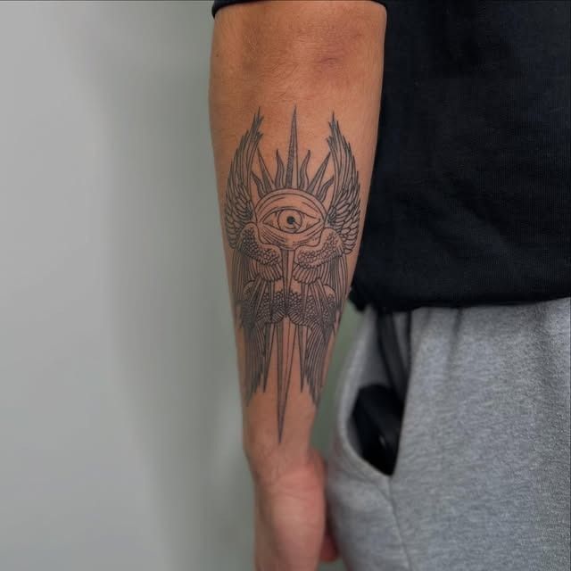 Tatuaje en el antebrazo de una persona: un ojo detallado con líneas negras y naranjas que irradian desde el centro.