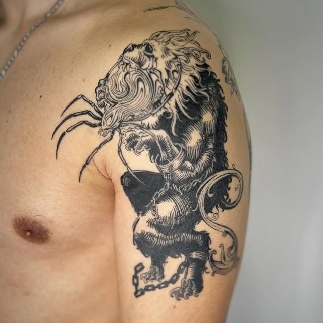 Tatuaje de león en blanco y negro en la parte superior del brazo y el pecho de una persona.