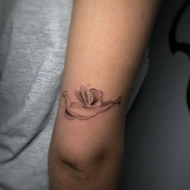 Primer plano de un brazo con un pequeño tatuaje de una flor dibujada con líneas negras cerca del codo.