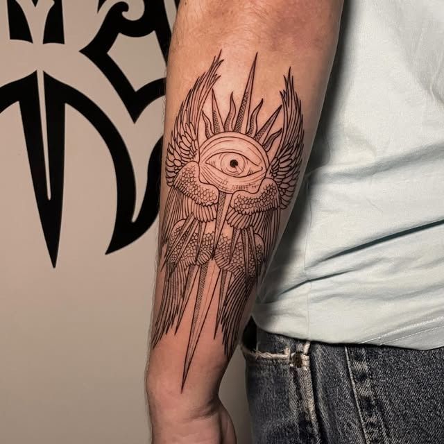 Tatuaje en el antebrazo de un ojo grande con rayos radiantes y detalles geométricos que recuerdan a alas.
