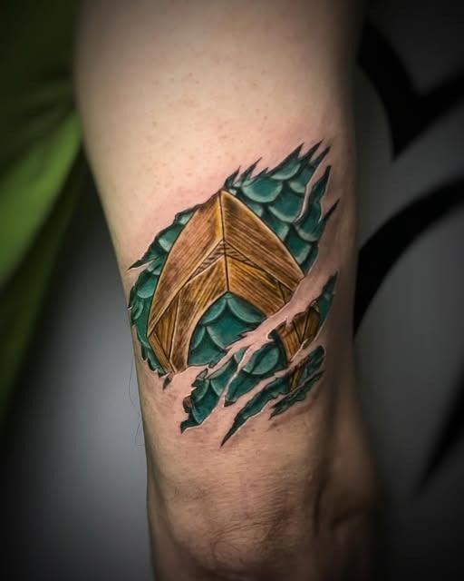 Primer plano de un tatuaje en la pierna con un diseño de dragón turquesa y criatura alada marrón.